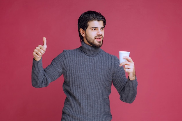 Man holding a disposable coffee cup and makes enjoyment sign.