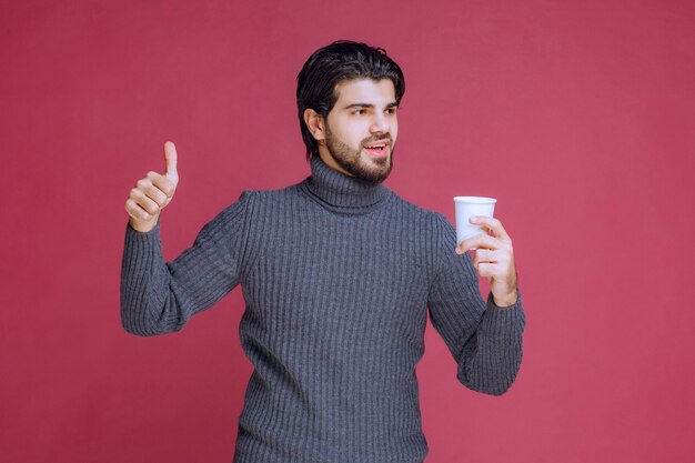 Man holding a disposable coffee cup and makes enjoyment sign.