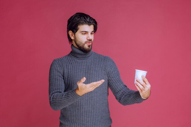 Man holding a disposable coffee cup and pointing at it.