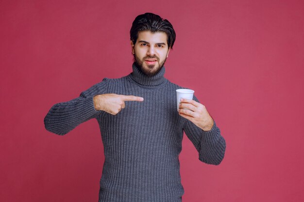 Man holding a disposable coffee cup and pointing at it.