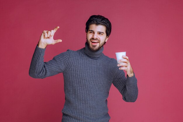 Man holding a disposable coffee cup and showing how much he needs.