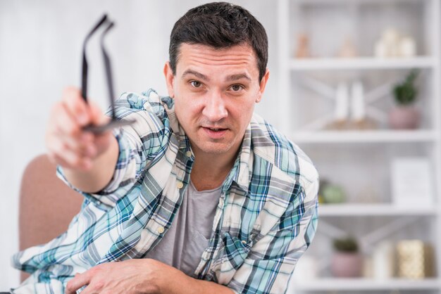 Man holding eyeglasses in stretched out hand on chair at home