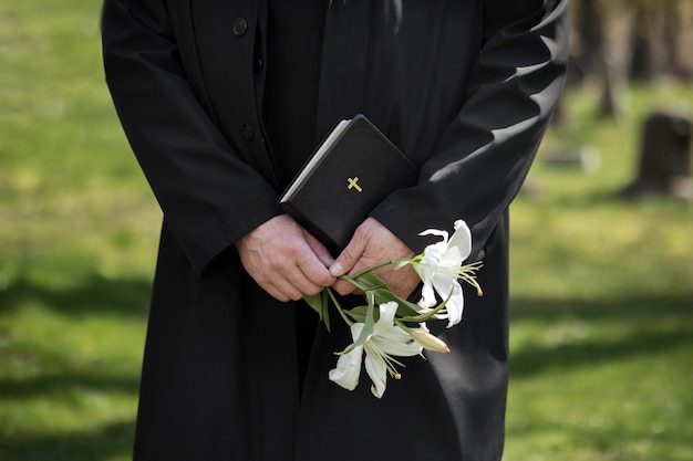 Мужчина держит цветы и библию на кладбище