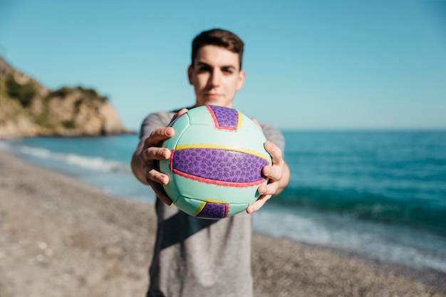 Free photo man holding football at the beach