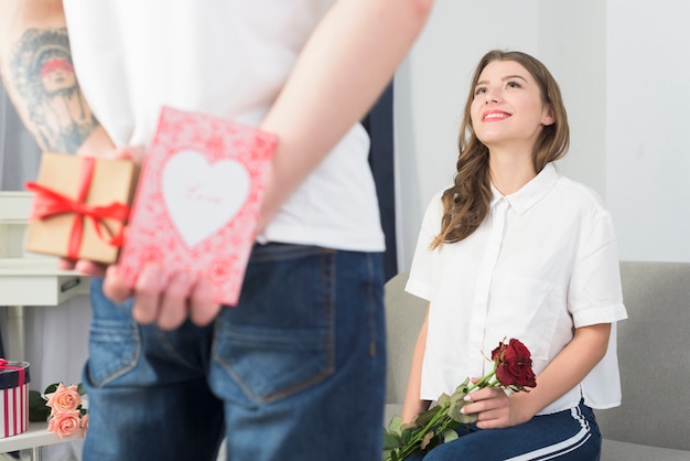 Man holding gift boxes for woman behind back