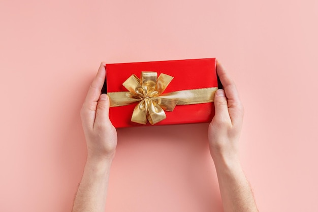 Free photo man holding giftbox with golden ribbon in hands on pink background