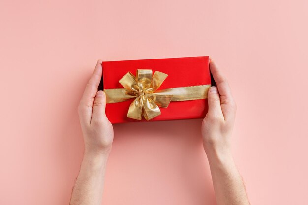 Man holding giftbox with golden ribbon in hands on pink background