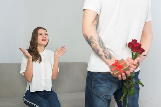 Man holding gifts for young woman behind back