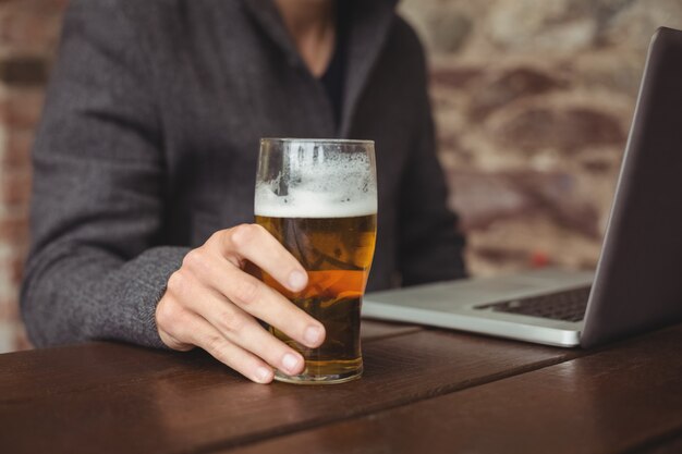 Man holding glass of beer and using laptop