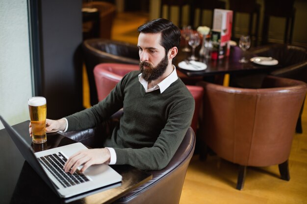 Man holding glass of beer and using laptop