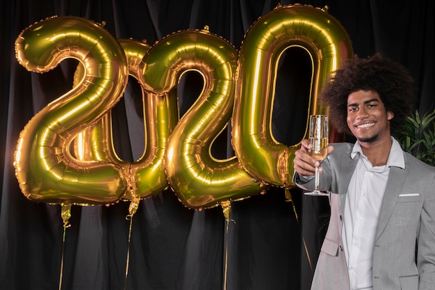 Мужчина держит бокал шампанского и воздушные шары с новым годом 2020