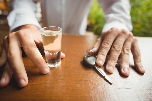 Free photo man holding glass of tequila shot and car key in bar counter