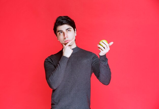 Man holding a green mandarin fruit and thinking