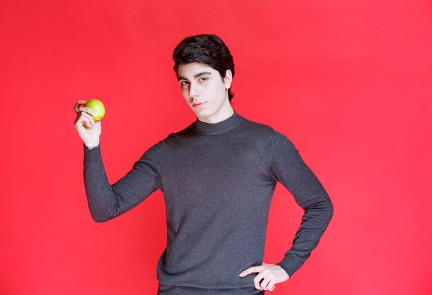 Man holding a green mandarin and pointing at it