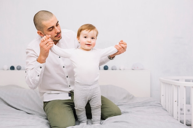 無料写真 男はベッドの上に立って面白い赤ちゃんの手を繋いでいます。