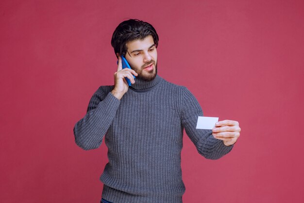 Man holding his business card and calling the contact number on it.