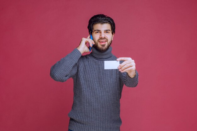 Man holding his business card and calling the contact number on it.