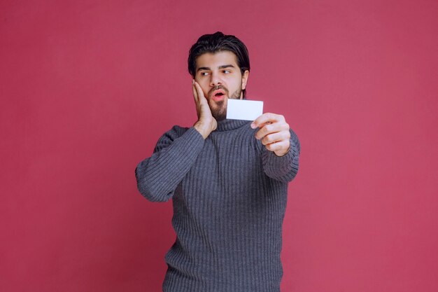 Man holding his business card and looks surprized.