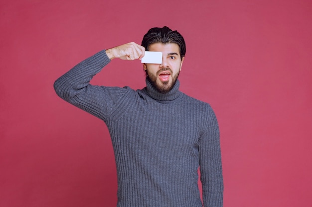 Free photo man holding his business card and putting it to his eye.