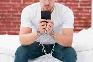 Free photo man holding his phone while he is tied up with chains