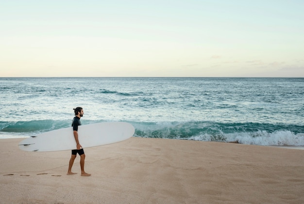 Foto gratuita uomo che tiene la sua tavola da surf vicino all'oceano