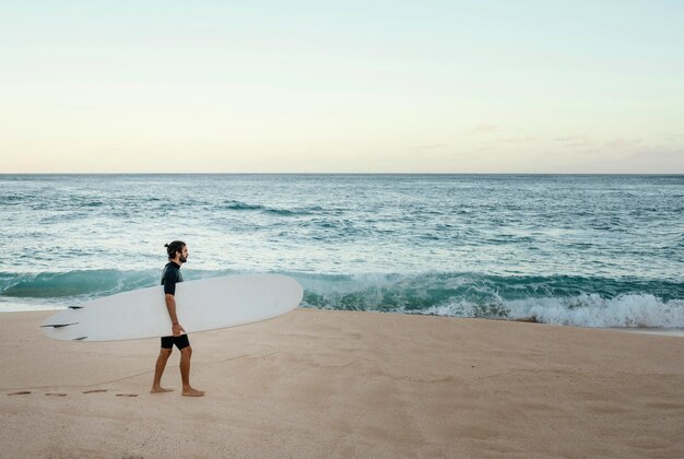 Man holding his surfing board next to the ocean