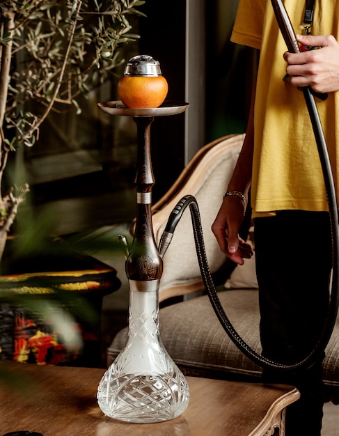 Free photo man holding hookah pipe placed on coffee table