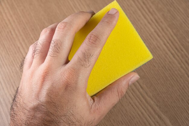 Man holding kitchen sponge on the wooden background