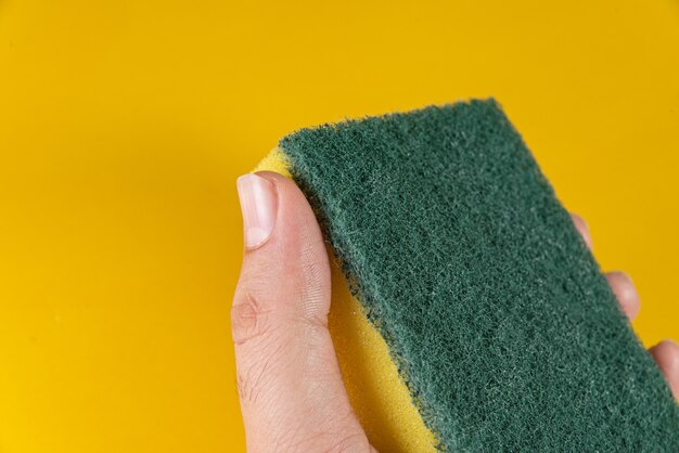 Man holding kitchen sponge on the yellow table