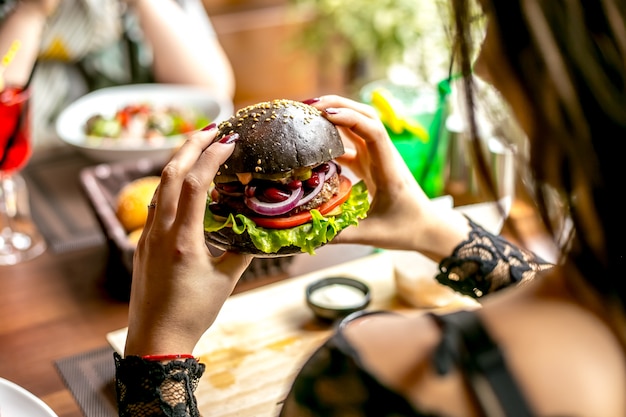 Man holding meat burger tomato onion lettuce beans side view