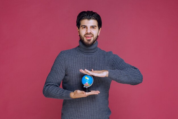Free photo man holding a mini globe between palms.