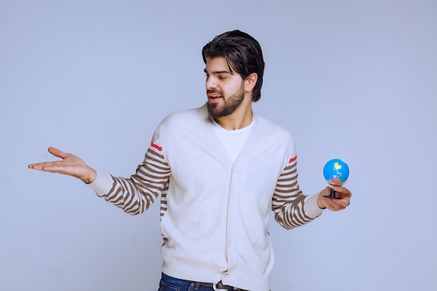 Free photo man holding a mini globe and pointing to something on the left.