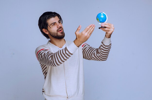 Man holding a mini globe, shaking it and trying to guess a location.