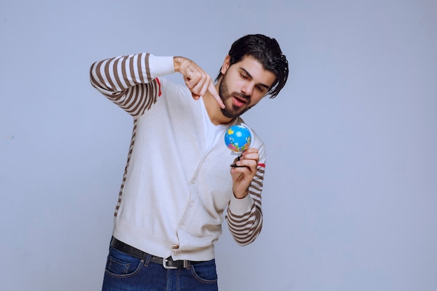 Foto gratuita uomo che tiene un mini globo, scuotendolo e cercando di indovinare una posizione.