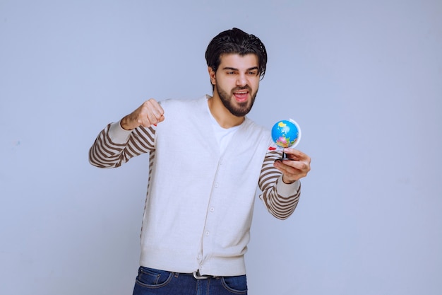 Uomo che tiene un mini globo, scuotendolo e cercando di indovinare una posizione.