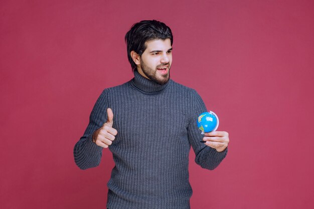 Человек, держащий мини-глобус и показывая большой палец вверх.