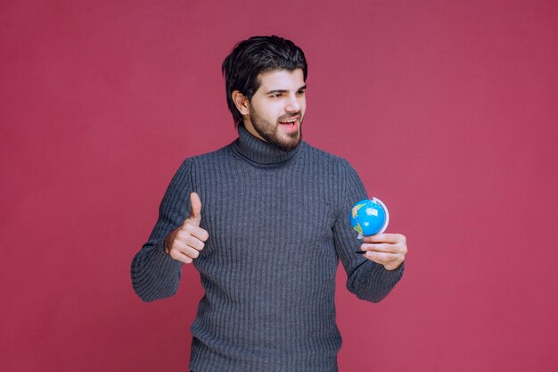 Man holding a mini globe and showing thumb up. 