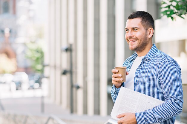 Man holding newspaper and coffee near building