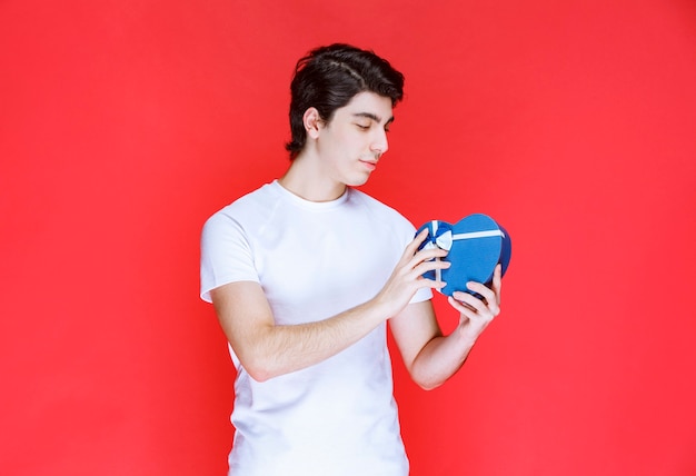 Man holding and offering a heart shape blue gift box. 