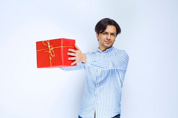 Мужчина держит или предлагает красную подарочную коробку своей девушке. Фото высокого качества