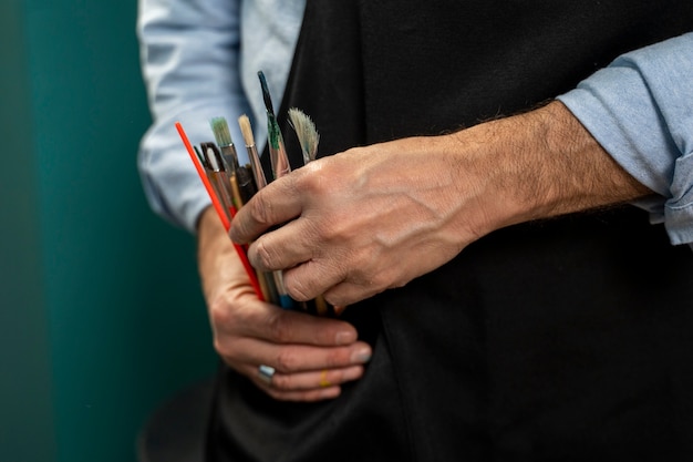 Free photo man holding painting brushes front view