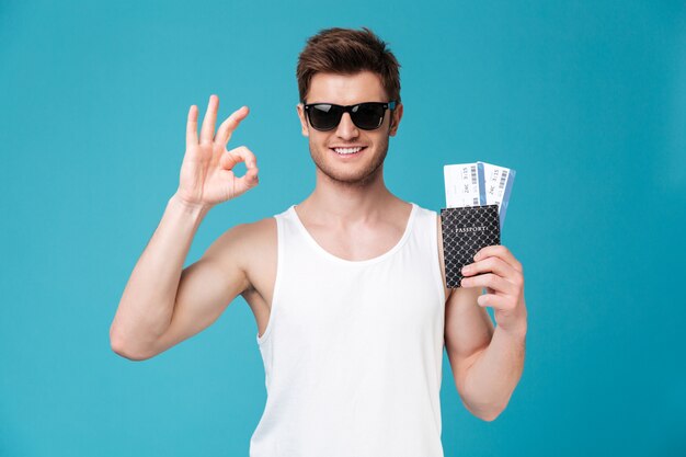 Man holding passport with flying tickets and showing ok gesture