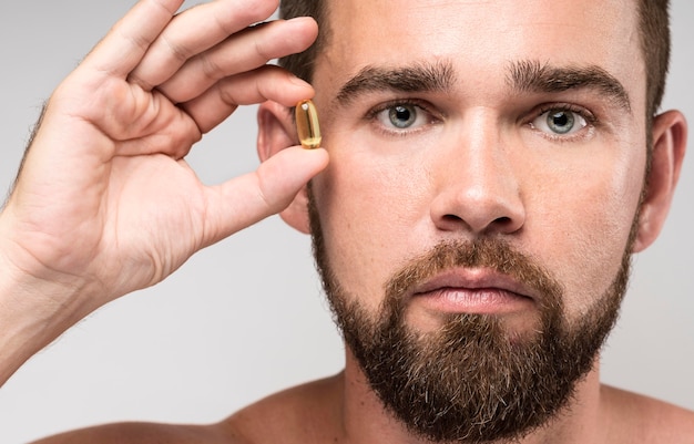 Free photo man holding a pill next to his face