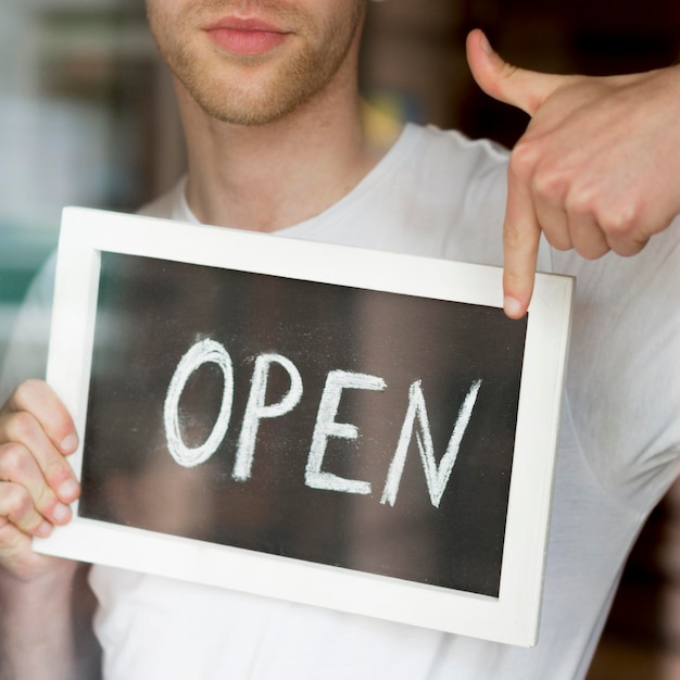 Free photo man holding and pointing at open coffee shop sign