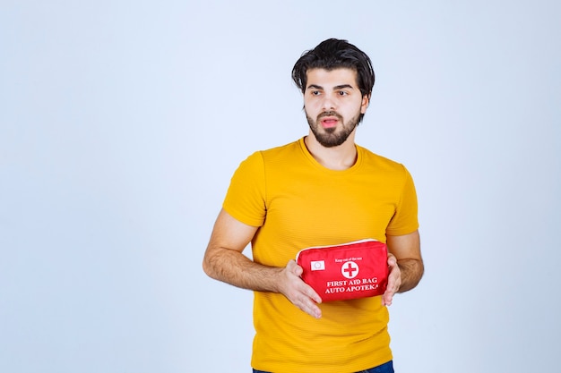 Man holding and promoting a red first aid kit.