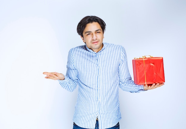 Man holding a red gift box and looks confused and thoughtful. High quality photo