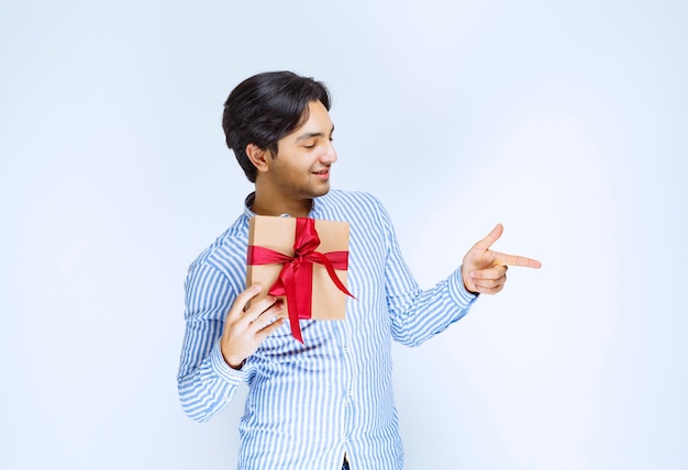Man holding a red ribbon cardboard gift box and pointing to someone. High quality photo