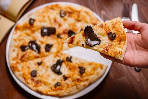 Man holding a slice of truffle pizza garnished with olive oil