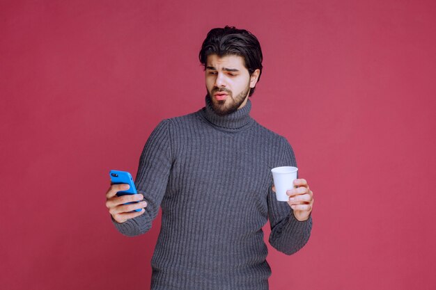 Man holding a smartphone and a coffee cup and looks confused.