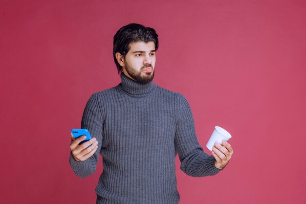 Man holding a smartphone and a coffee cup and looks confused.